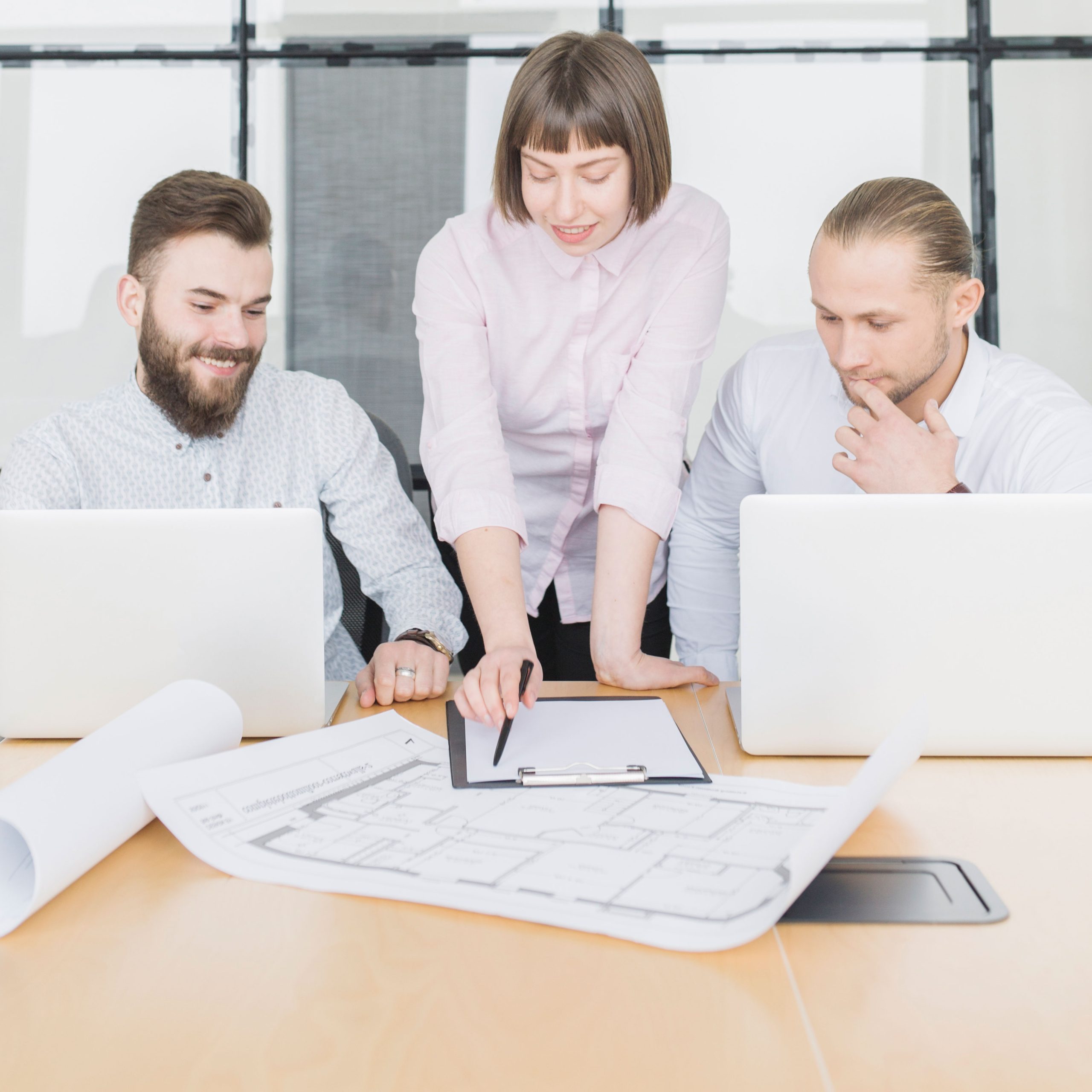 archicad-vs-revit-software-vergleich-team Planungsteam mit Laptops bespricht einen Grundrissplan – Revit Kosten beim Umstieg abwägen